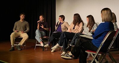 Sechs überwiegend junge Frauen und ein Mann auf einer Bühne sitzend vor einer Filmleinwand